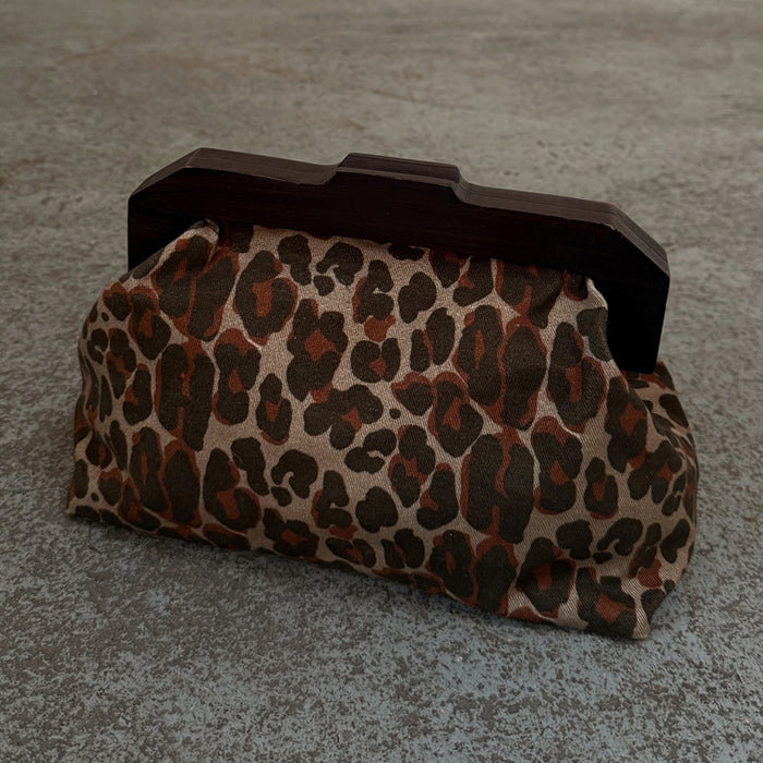Lucia Leopard Denim Bag featuring an iconic leopard print and a dark wooden handle in a clutch style.
