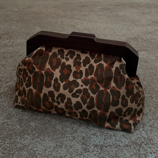 Lucia Leopard Denim Bag featuring an iconic leopard print and a dark wooden handle in a clutch style.