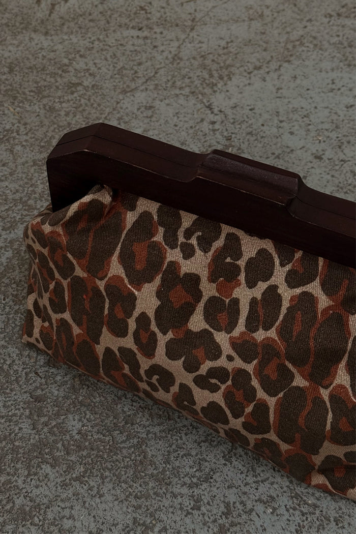 Lucia Leopard Denim Bag with a leopard print and dark wooden handle, resting on a textured surface.