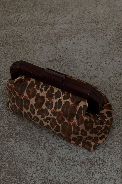 Lucia Leopard Denim Clutch Bag featuring an iconic animal print and a dark wooden handle on a textured ground.