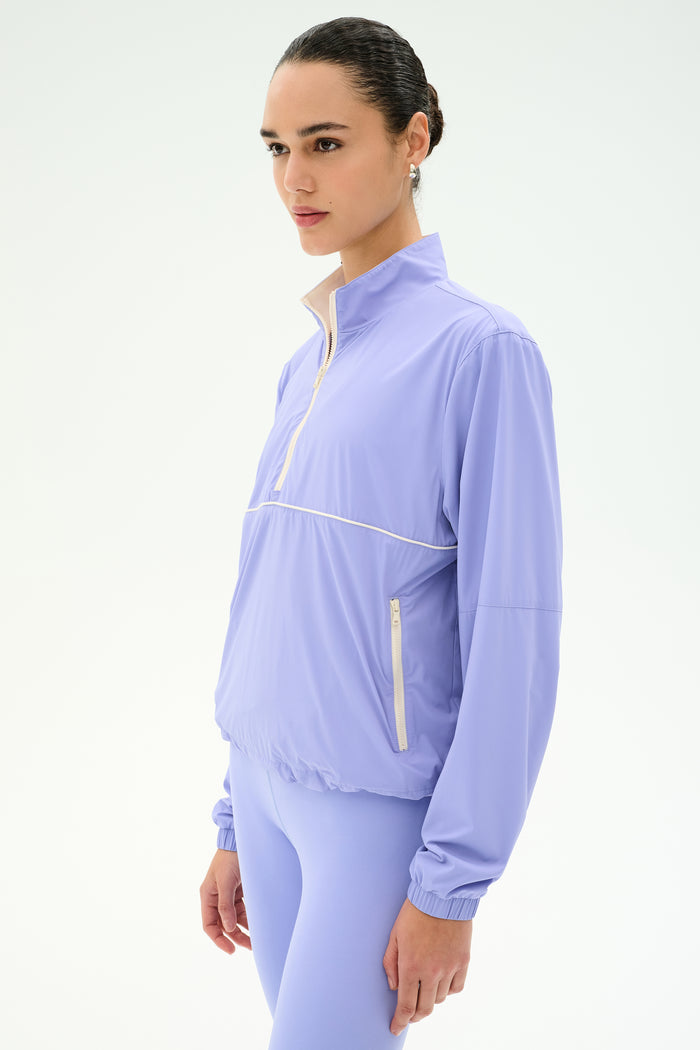 A person wearing the SPLITS59 Lyle Woven Nylon Pullover in Purple Haze/Creme stands against a plain white background, looking forward.