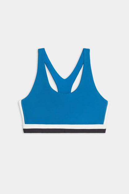 The SPLITS59 Maci Airweight Bra in Stone Blue/Graphite features racerback straps and white and black trim along the bottom band, shown against a plain white background.