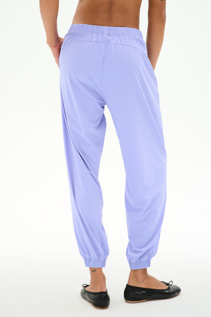 Person wearing SPLITS59 Megan Woven Nylon Jogger in Purple Haze and black ballet flats, shown from the back against a plain white background.