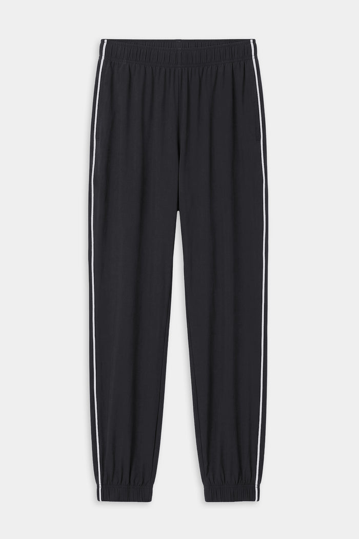 The SPLITS59 Megan Woven Nylon Jogger w/ Piping in black/creme features an elastic waistband and cuffs, white piping down each leg, and is made from an 85% nylon blend. Shown on a plain white background.