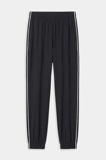 The SPLITS59 Megan Woven Nylon Jogger w/ Piping in black/creme features an elastic waistband and cuffs, white piping down each leg, and is made from an 85% nylon blend. Shown on a plain white background.