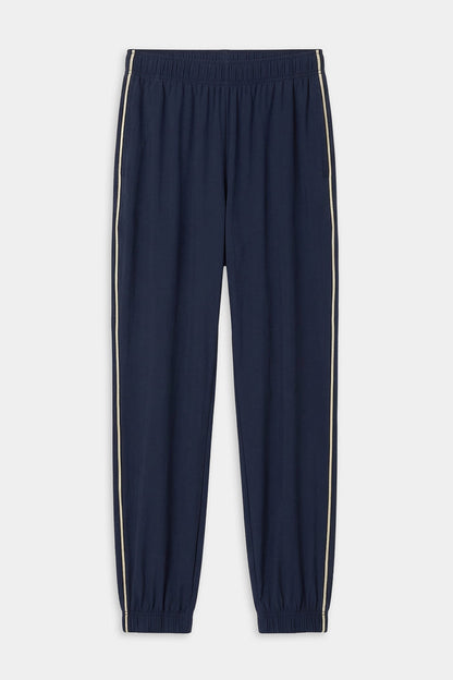 The SPLITS59 Megan Woven Nylon Jogger w/ Piping in Indigo/Creme features an elastic waistband and cuffs, white side piping, and is crafted from stretchy fabric for comfort and flexibility.