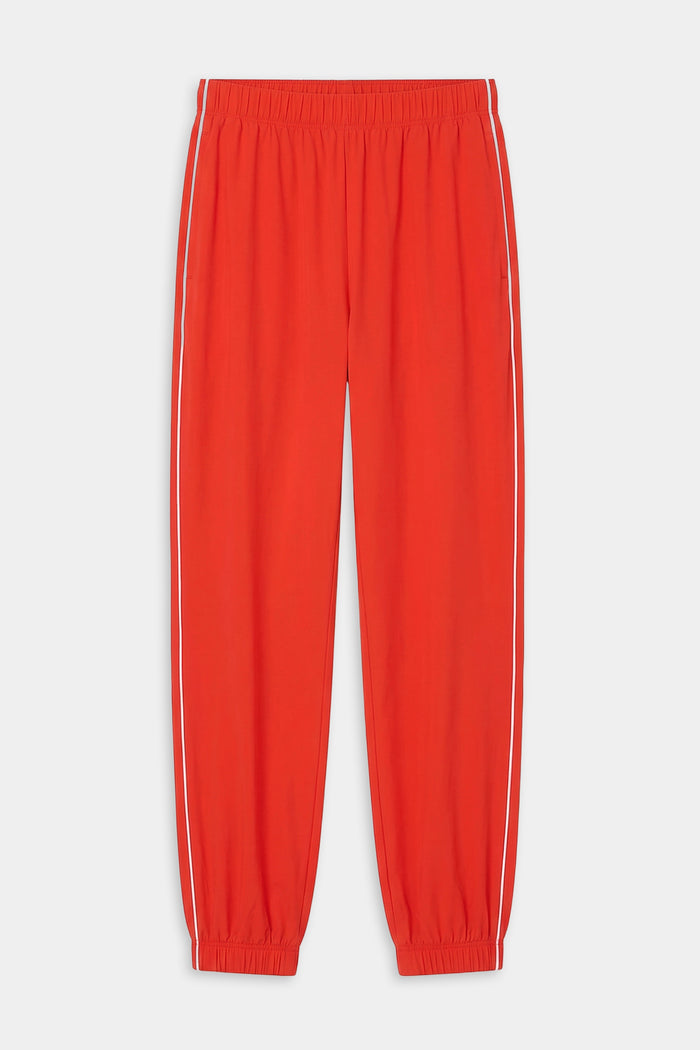 The SPLITS59 Megan Woven Nylon Jogger w/ Piping in Lotus Red/Creme features white side piping, an elastic waistband, and elastic cuffs. Crafted from a spandex-nylon blend and shown laid flat on a white background.