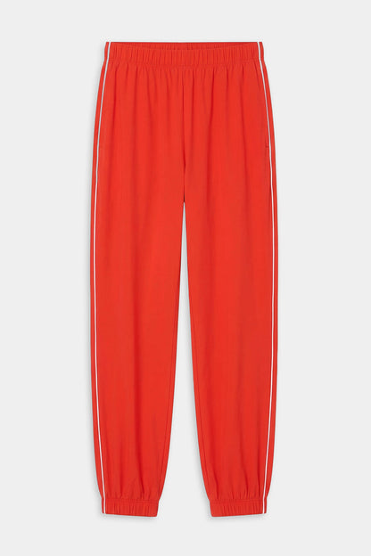 The SPLITS59 Megan Woven Nylon Jogger w/ Piping in Lotus Red/Creme features white side piping, an elastic waistband, and elastic cuffs. Crafted from a spandex-nylon blend and shown laid flat on a white background.