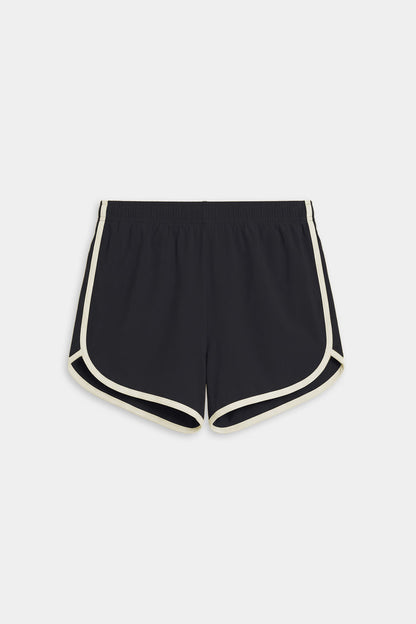 The SPLITS59 Megan Woven Nylon Run Short in Black/Creme features white trim, an elastic waistband, and curved hems in a nylon-spandex blend, shown laid flat on a white background.