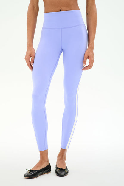 A person wears SPLITS59 Miles High Waist Rigor 7/8 leggings in Purple Haze/White with black ballet flats, standing against a plain white background.