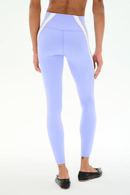 Model wears SPLITS59 Miles High Waist Rigor 7/8 leggings in Purple Haze/White, paired with black ballet flats and small ankle tattoos, standing against a plain white background—ideal for yoga or gym workouts.