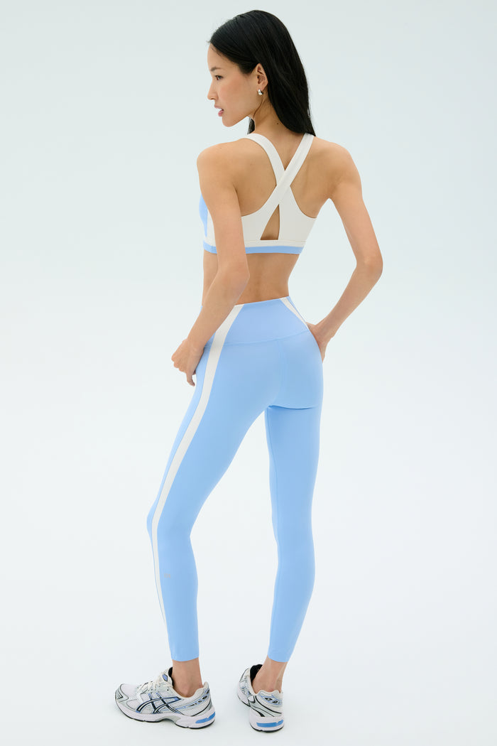 A woman faces away, wearing the SPLITS59 Miles High Waist Rigor 7/8 set in Skylight/White with white sneakers, against a plain light background.
