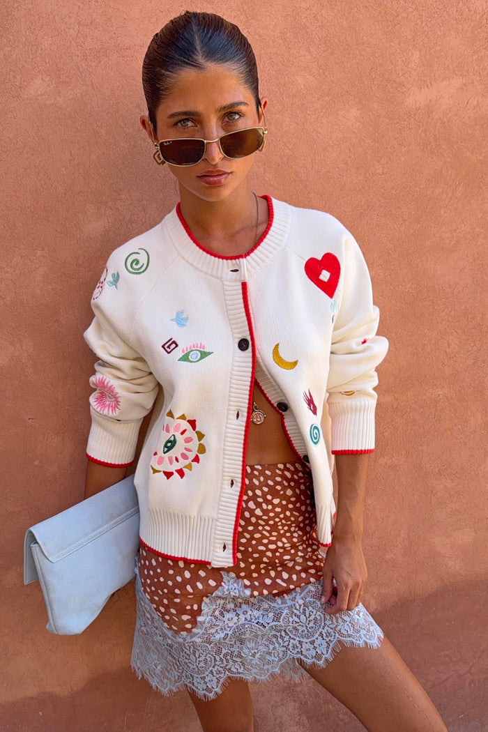 Cream Morocco Charms Cheryl Cardigan with red trim and iconic motifs, styled with a spotted lace-trim skirt and clutch.
