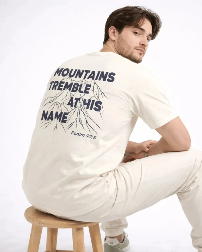Man wearing a white long-sleeve shirt with text and graphics on the back, sitting on a wooden stool against a white background.