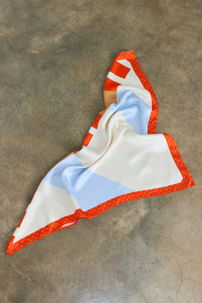 Multi Stripe Mix Bandana featuring bold orange and blue stripes and a polka dot border, draped on a grey concrete floor.