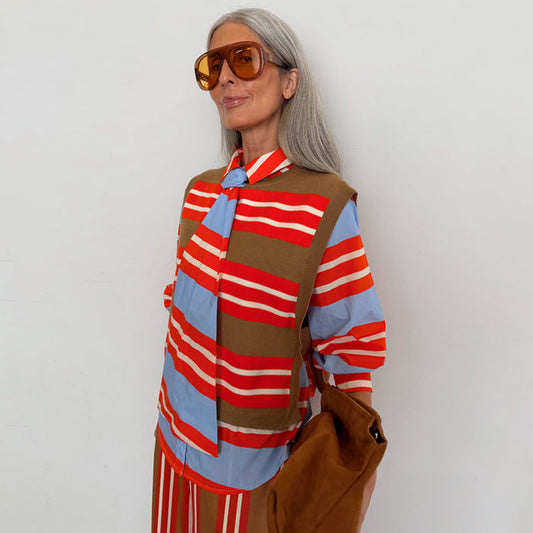 Multi Stripe Tank Top in tan and red knit, layered over a blue striped shirt on a model with silver hair.
