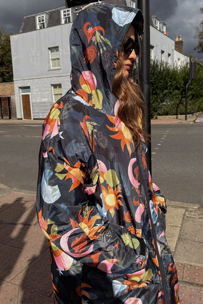 Navy Charm Coat with a colourful sun and moon print, waterproof fabric and hood, worn in an outdoor street setting.