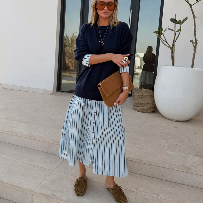 Navy Knit Jumper Dress with a blue stripe cotton skirt, styled with a tan suede clutch for a casual London look.