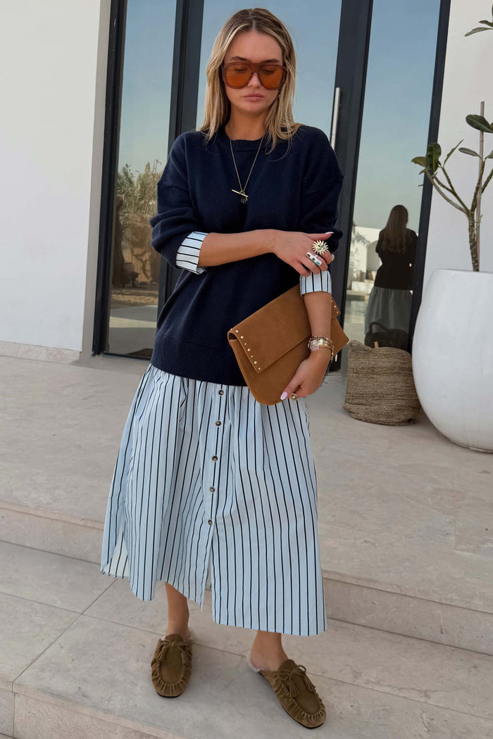 Navy Knit Jumper Dress with a blue striped cotton skirt, accessorised with a brown suede clutch and sunglasses.
