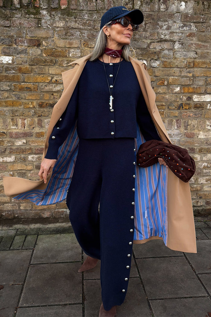 Navy Studded Knit Jogger co-ord with silver side studs, styled with a camel trench coat, navy cap and sunglasses.