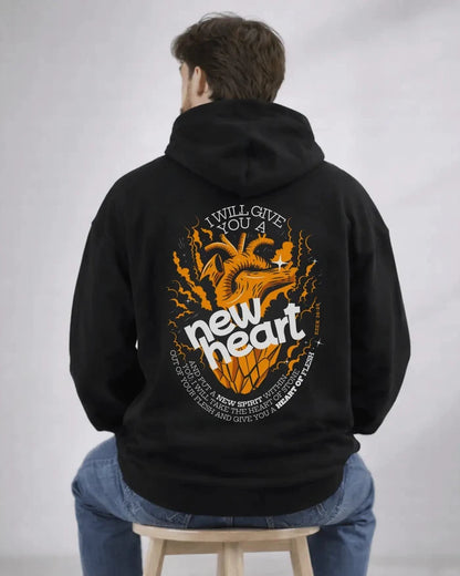 Person wearing a black hoodie with a graphic design on the back, sitting on a stool against a plain background.
