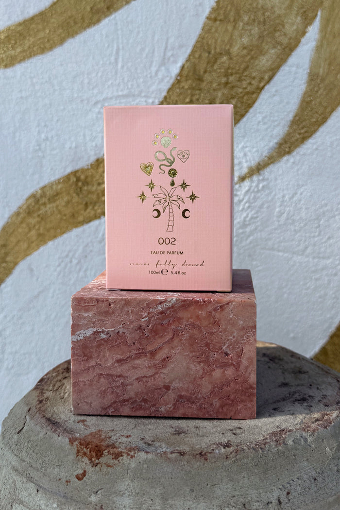 NFD Eau De Parfum 002 pink box with gold foil tropical icons, displayed on a pink marble block.
