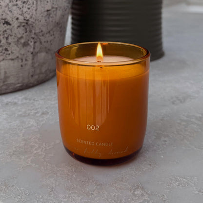 NFD Scent 002 Eau De Parfum Candle in an amber glass jar with a lit flame and white NFD branding.