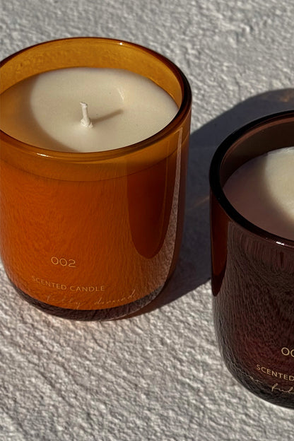 NFD Eau De Parfum Candle 002 in an orange glass jar, displayed on a textured white surface in bright natural sunlight.