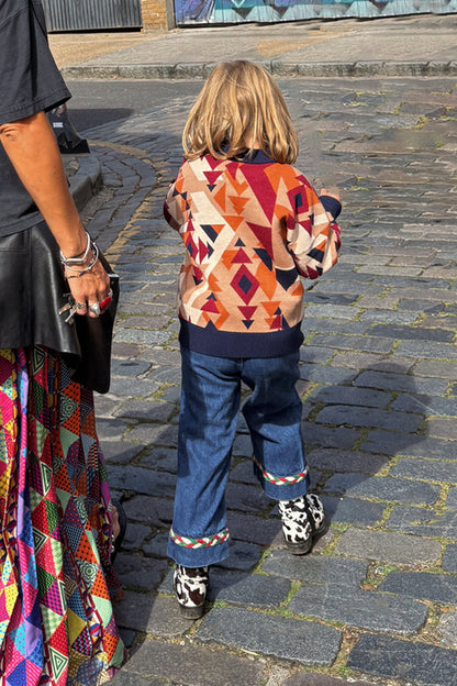 Geometric NFD Kids Aspen Jumper in orange, navy and tan worn by a child walking on a cobblestone street.