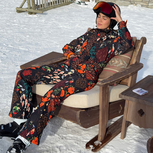 Night Garden Ski Suit featuring leopard and poppy prints, worn by a woman lounging at a snowy ski resort.
