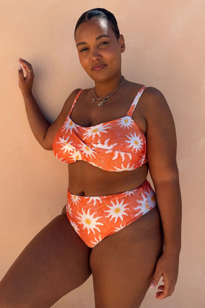Orange Sun High Waist Bikini Brief with iconic sun motifs and a fine line print on a model leaning against a wall.