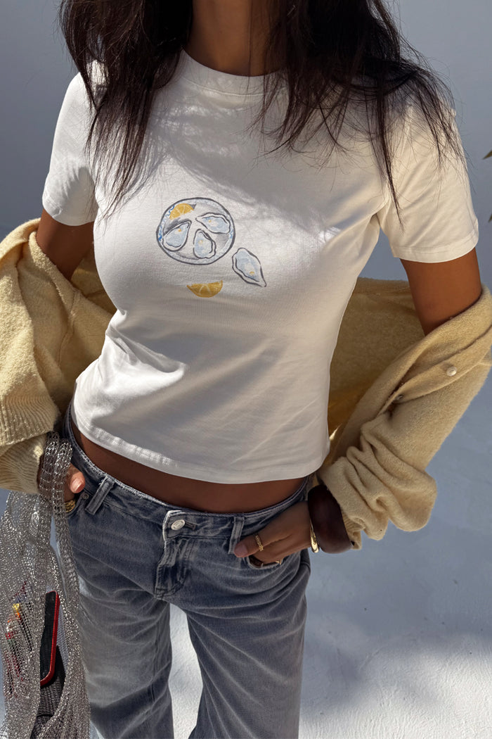 White Oyster Baby T Shirt featuring a fine line oyster and lemon print, styled with blue jeans and a yellow cardigan.