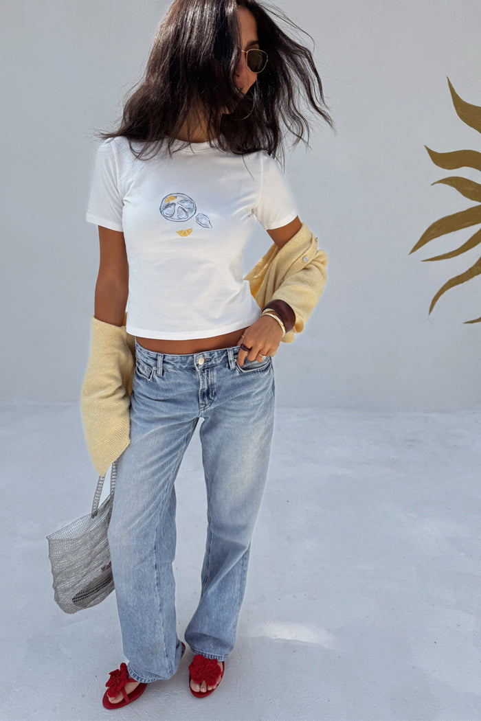 White Oyster Baby T Shirt with oyster and lemon print, styled with blue jeans, a yellow cardigan and red sandals.