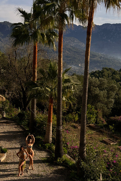Palm Cupped Bikini Top with a green leaf print, worn by two models in a Mediterranean garden with palm trees.