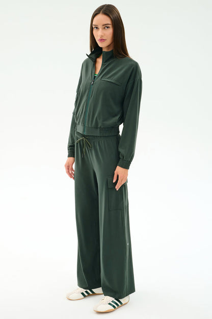 A woman stands in a relaxed pose wearing the SPLITS59 Peaches Airweight Cargo Jacket in Military and matching wide-leg pants, paired with white sneakers against a plain light background.