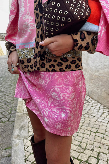 Pink Bandana Mini Dorris Skirt featuring a white paisley print, styled with a leopard print cardigan on a cobbled street.