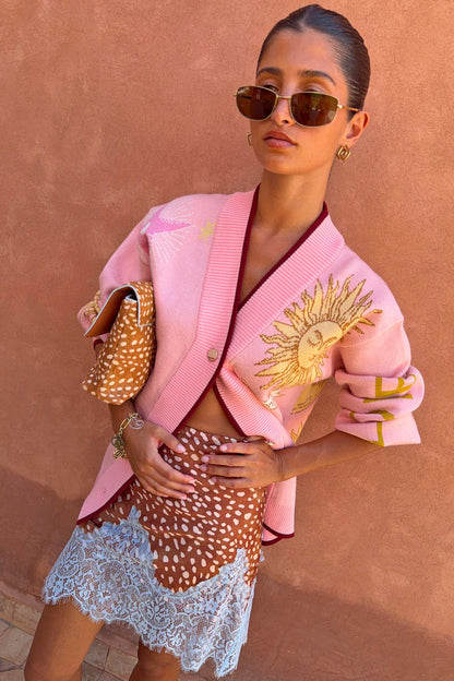 Pink Mystical Cardigan in a soft knit with a sun jacquard motif and burgundy trims, paired with a patterned lace skirt.