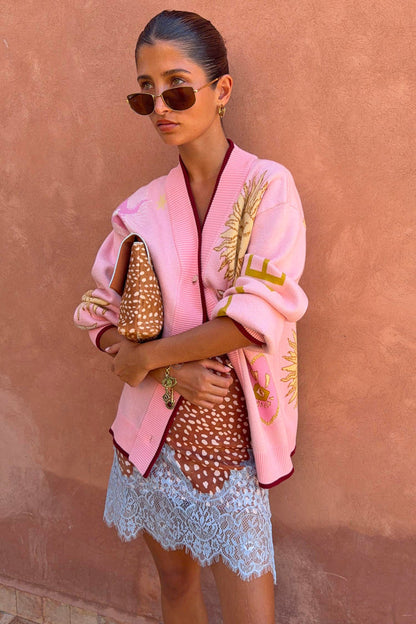 Pink Mystical Cardigan with jacquard sun and moon motifs and burgundy trims, styled with a lace-trimmed dress.