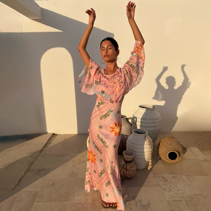 Pink Sun Anais Dress with iconic soleil motifs, sheer draped top and satin-esque bias skirt in a sun-drenched courtyard.
