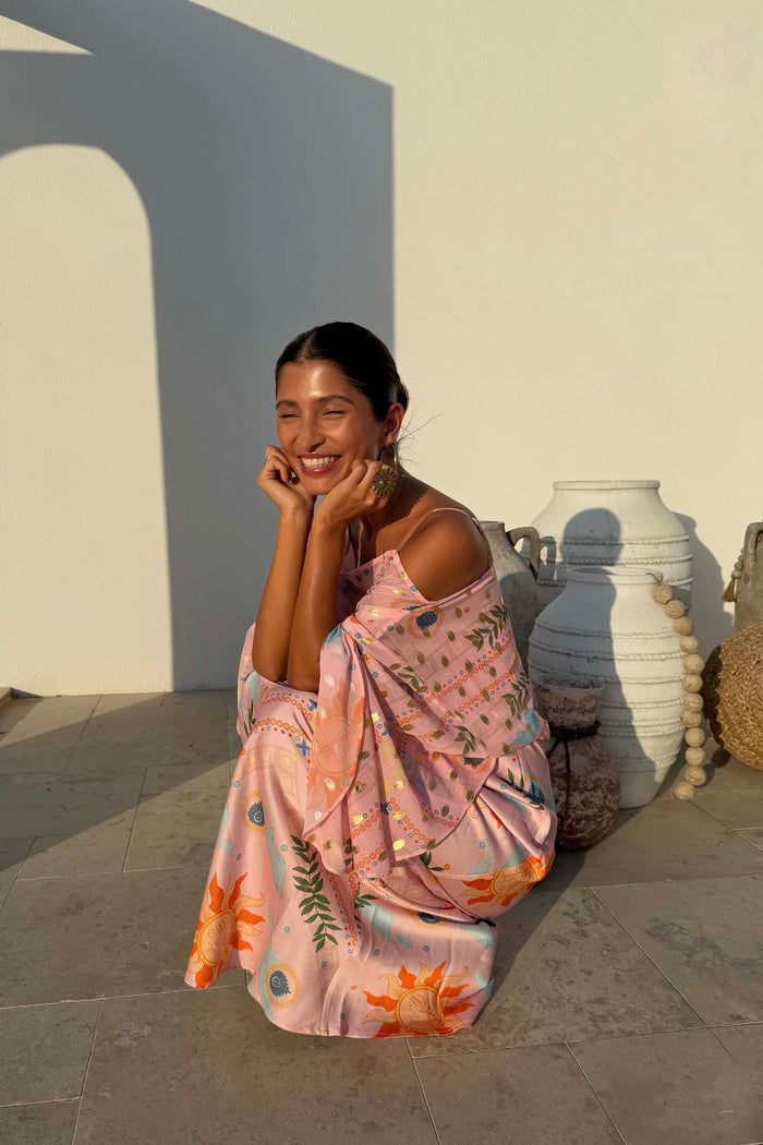 Pink Sun Anais Dress with iconic soleil motifs and gold flecks, shown on a model crouching by white vases.