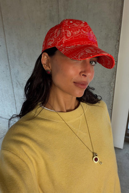Red Bandana Cap in a cotton paisley print with an embroidered NFD logo, worn by a model in a yellow sweatshirt.