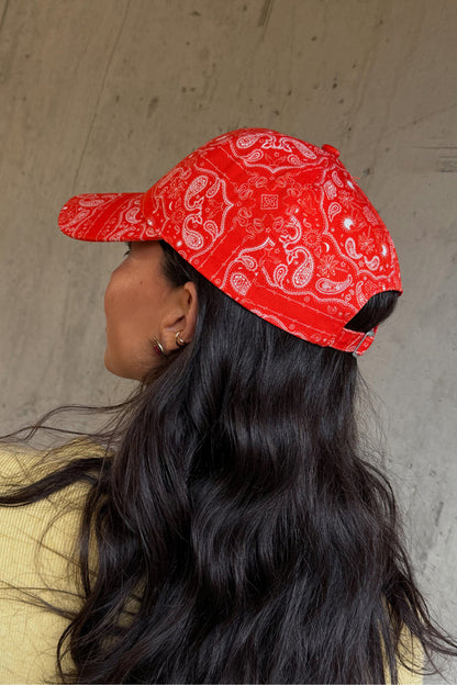 Red Bandana Cap featuring a white paisley print and adjustable strap, shown from the side on a model.
