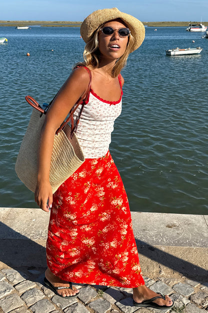 Red Floral Midi Skirt and floral pointelle vest with a straw hat, bag, and sunglasses for a summer vacation look.