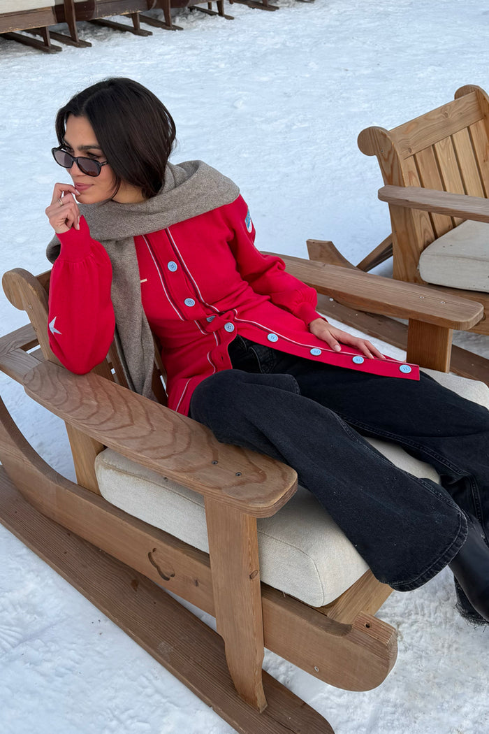 Red Ski Knit Long Cardigan with blue buttons and tie waist, designed in London and styled in a snowy setting.