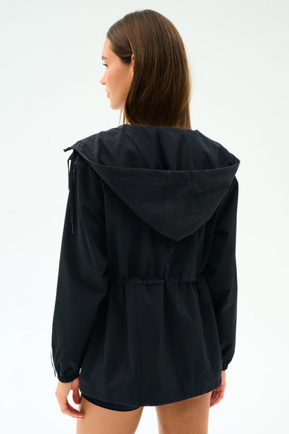 A woman faces away, wearing the SPLITS59 Reggie Water Repellent Jacket in black/white, featuring a cinched waist and sleek nylon fabric.