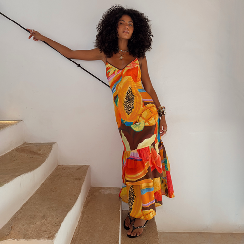 Rio Laragh midaxi dress in cotton-linen with a tropical papaya print and tiered hem, worn by a model on stairs.