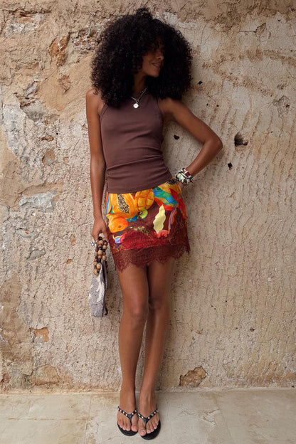 Rio Mini Maeva Skirt in a tropical fruit print with brown lace trim, styled with a brown vest for a summer vacation look.