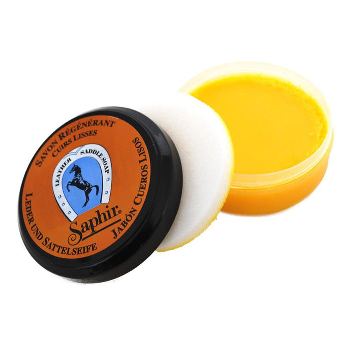 A jar of Saphir Etalon Noir saddle soap with a black lid and orange label show included sponge, indicating it is a leather cleaning product.