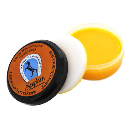 A jar of Saphir Etalon Noir saddle soap with a black lid and orange label show included sponge, indicating it is a leather cleaning product.