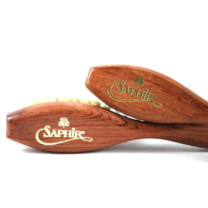 A long-handled spatula-shaped shoe polish applicator brush with black & neutral bristles and a wooden handle.
